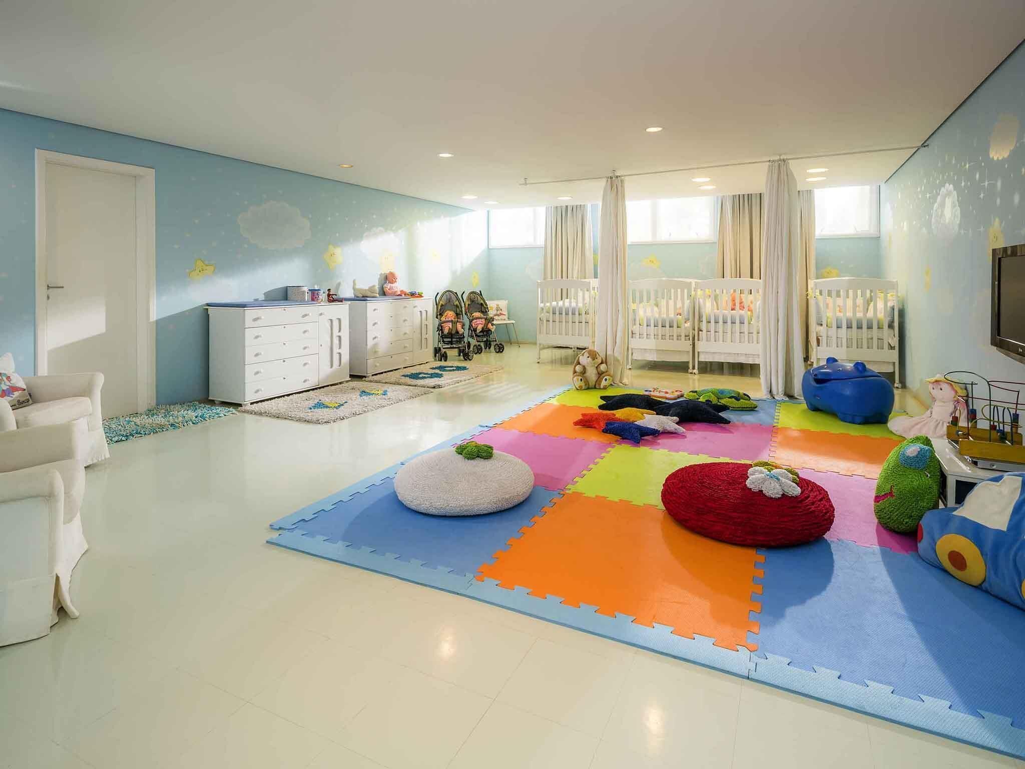A child's playroom with a colorful play mat, white furniture, and a crib.