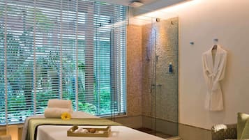 Relax in a serene spa room with a spacious bed, glass shower enclosure, and wicker chair.
