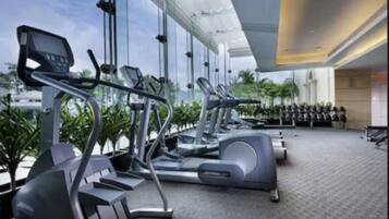 Ein modernes Fitnessstudio mit Laufbändern, Ergometer und einem großen Fensterbereich mit Blick auf Palmen.