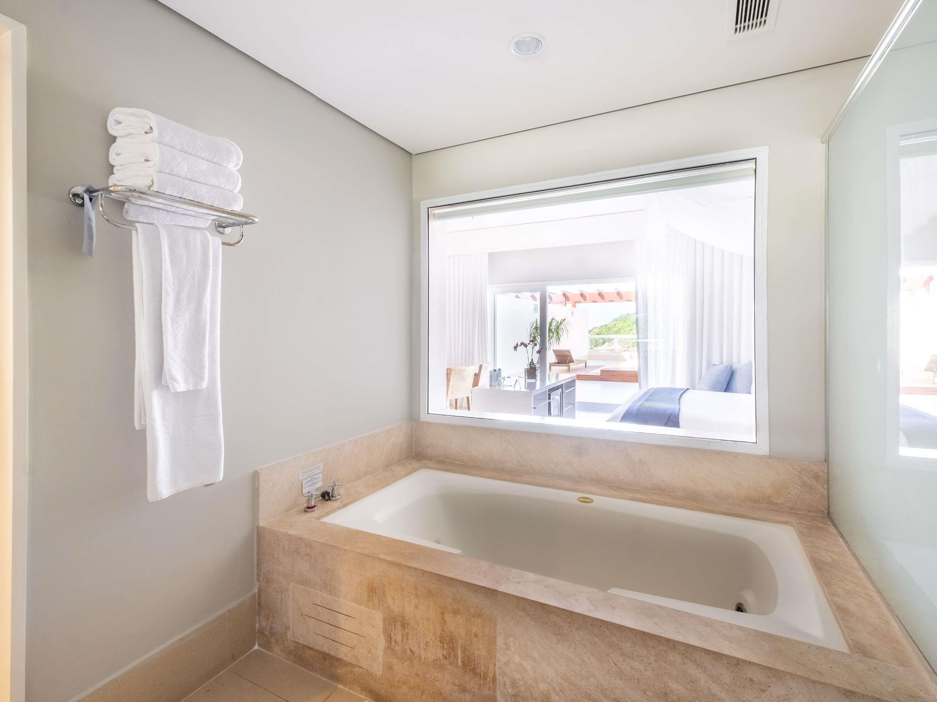Un baño moderno con una bañera grande, un perchero con toallas dobladas y una ventana con vistas a un patio exterior.