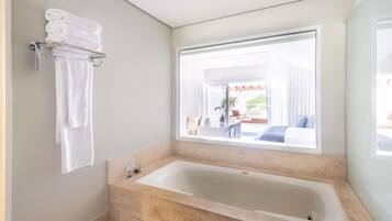 Un baño moderno con una bañera grande, un perchero con toallas dobladas y una ventana con vistas a un patio exterior.