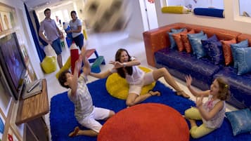Un salon moderne avec une moquette bleue à longs poils, un pouf rond rouge et un canapé coloré agrémenté de coussins à motifs.