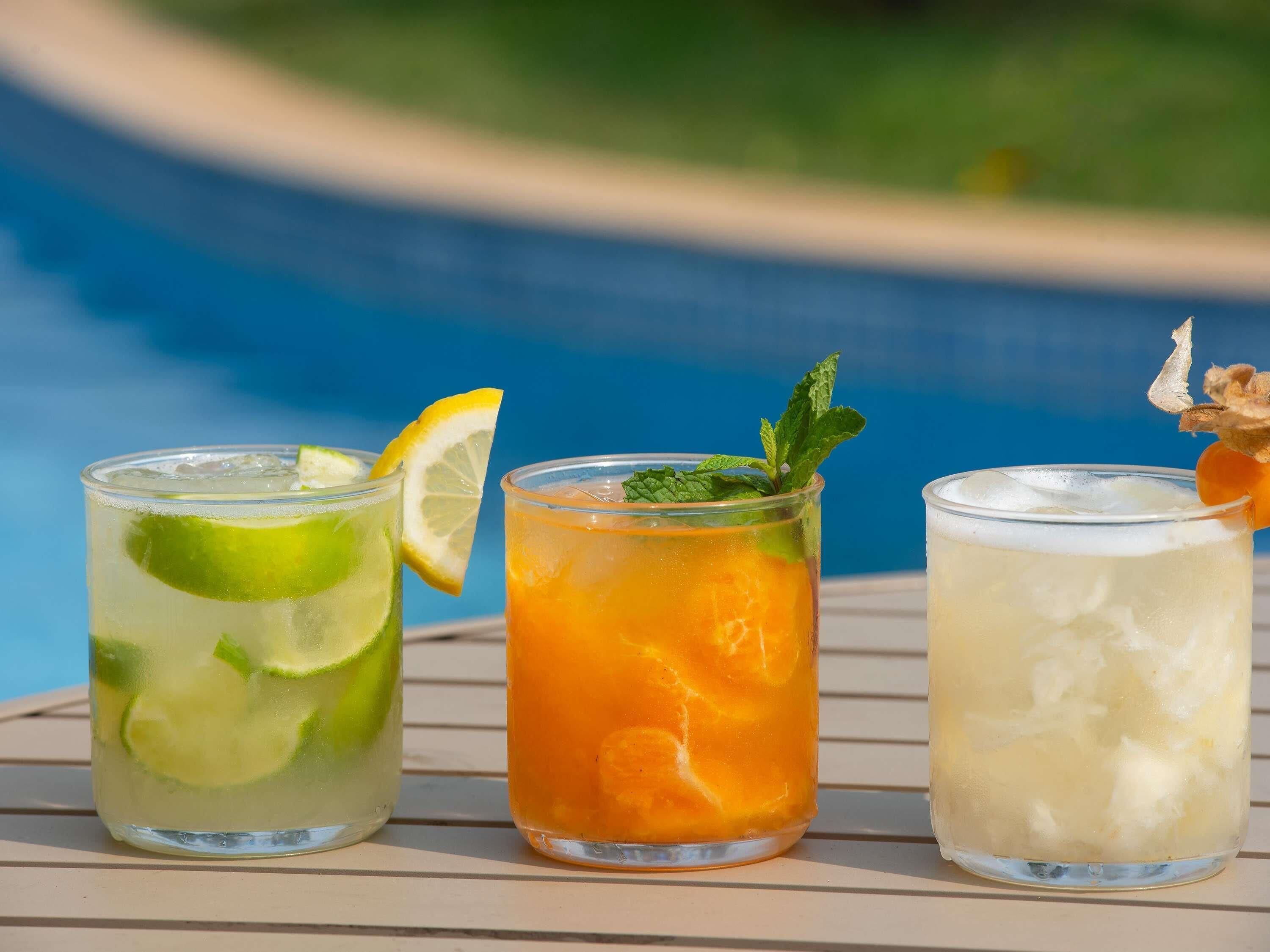 Three glasses of beverages on a table by a pool.