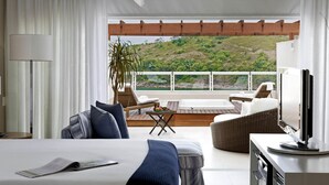 A hotel room with a bed, a TV, a balcony with a view of a hillside, and a dining area with a table and chairs. - Hotel Jequitimar Guarujá Resort & Spa by Accor (Guarujá)