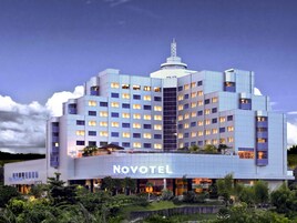 Un hotel moderno con varios pisos, un llamativo letrero de 'NOVOTEL' y una antena en la azotea.