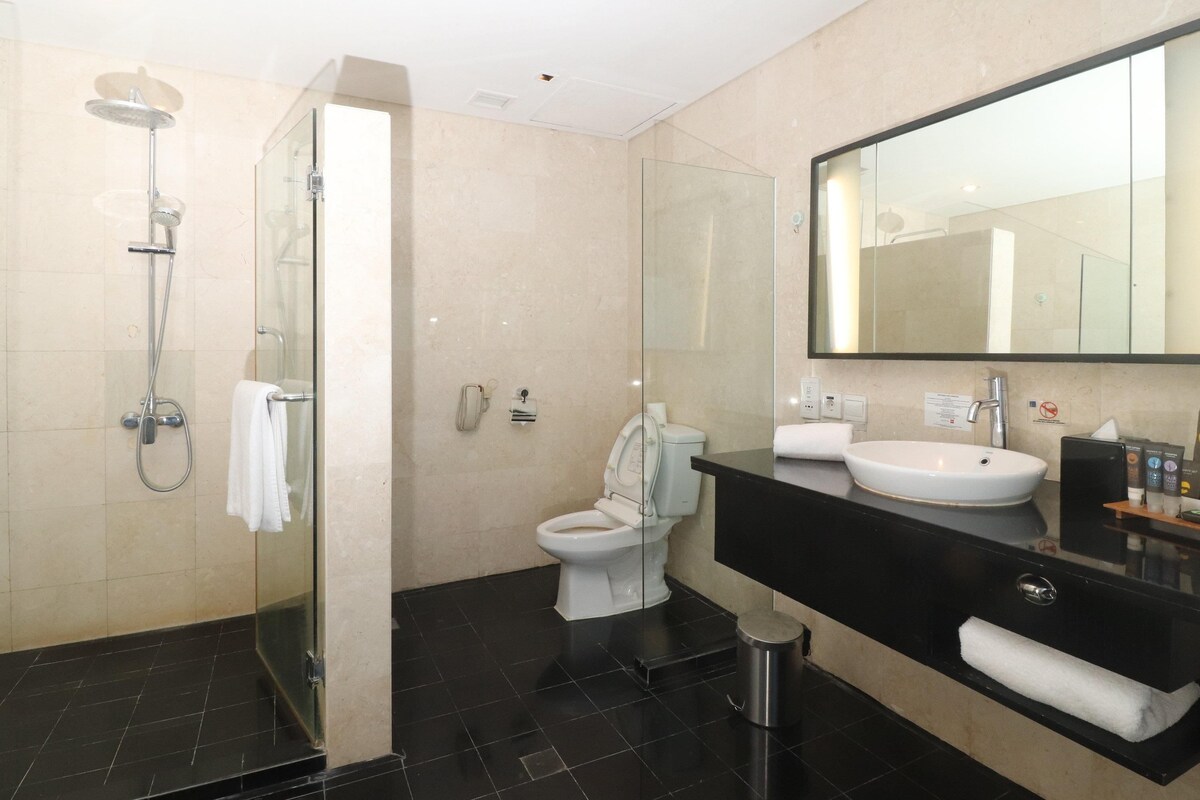 Un baño moderno con ducha de vidrio, inodoro, lavabo y un espejo grande.