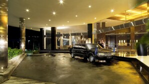 A modern hotel entrance with a black limousine parked in the driveway.