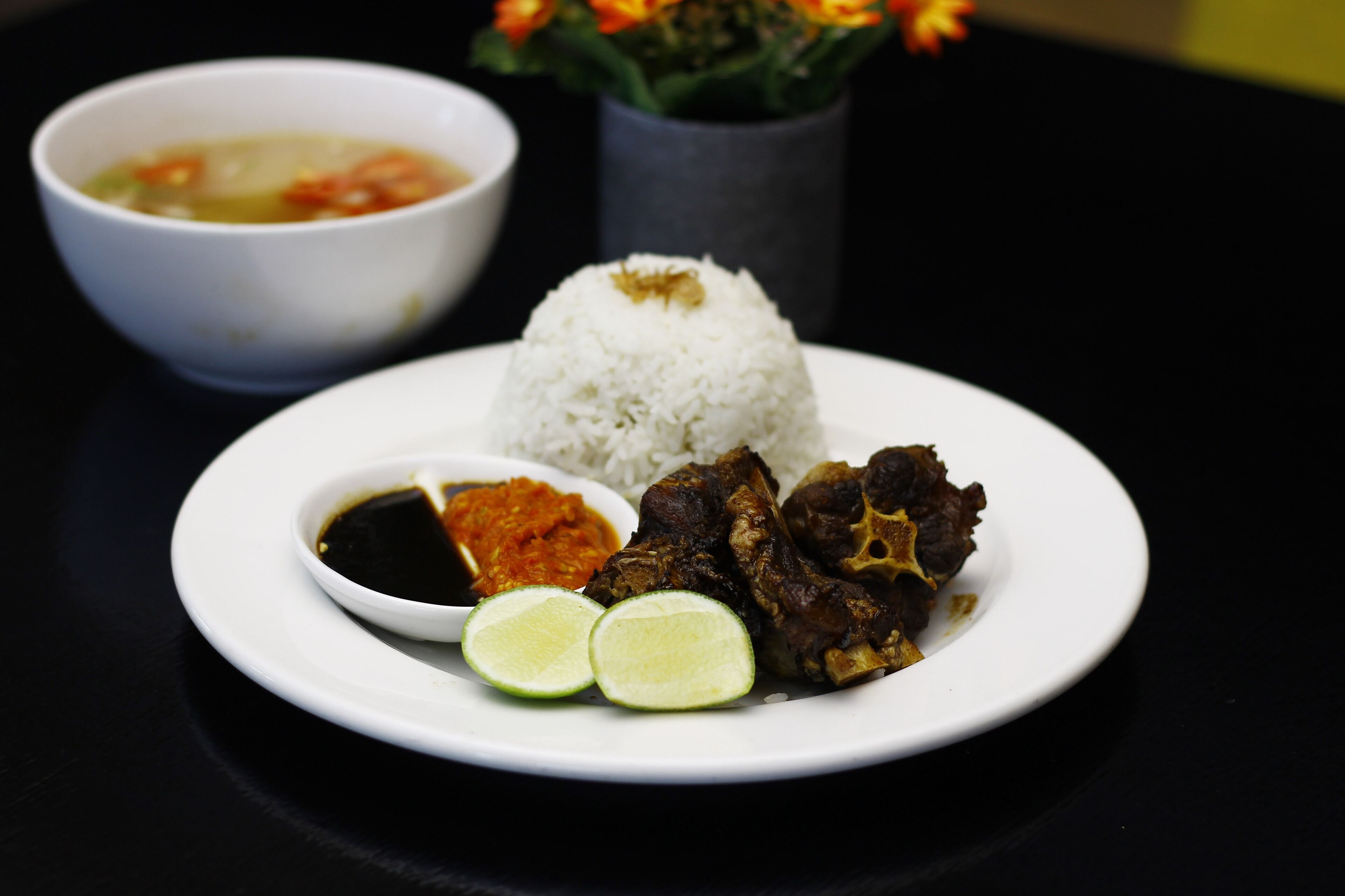 A plate with white rice, grilled meat, lime slices, and a small bowl of sauce.