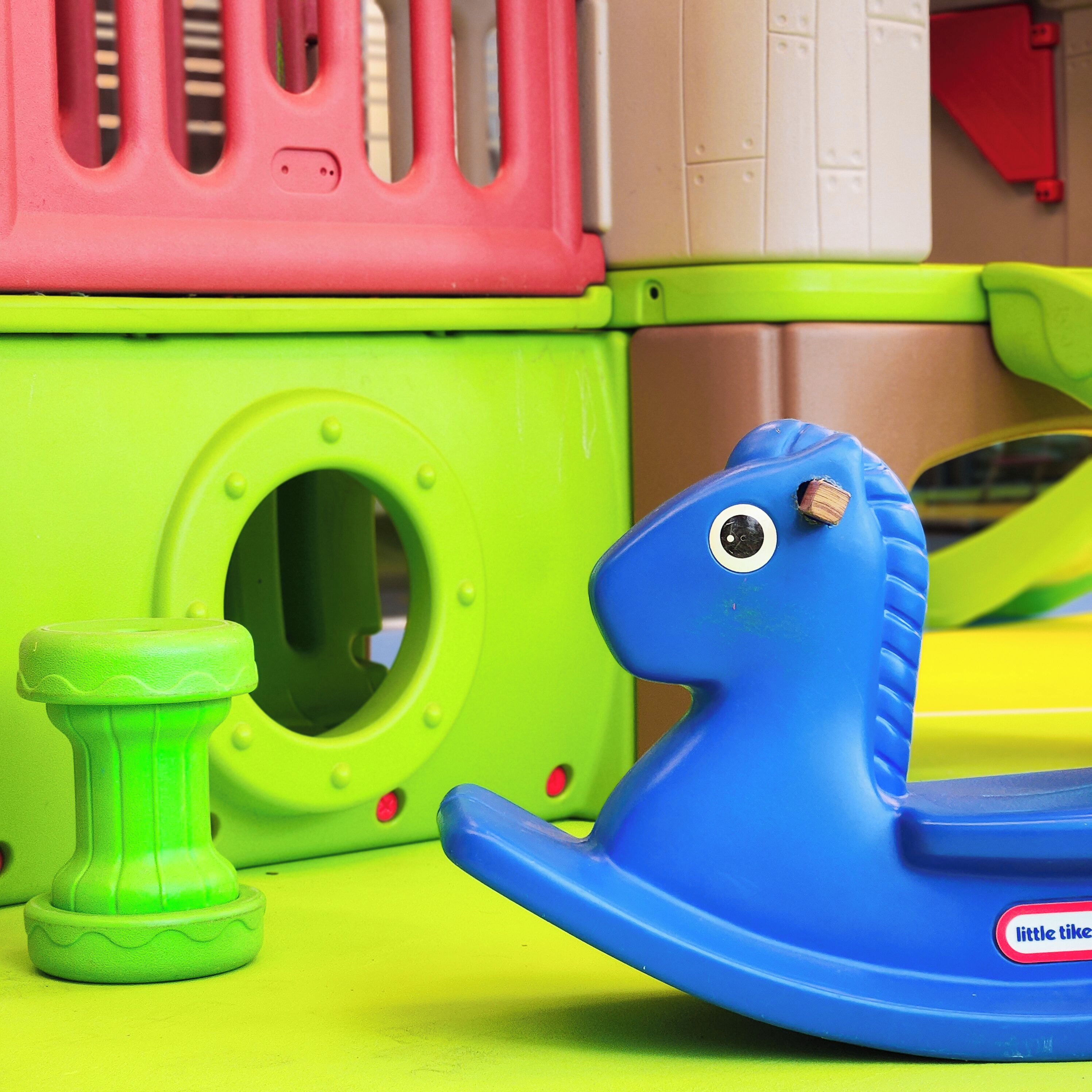 Een kinderspeelgoed met een blauwe romp en een rode bovenkant, op een oppervlak van groen en geel.