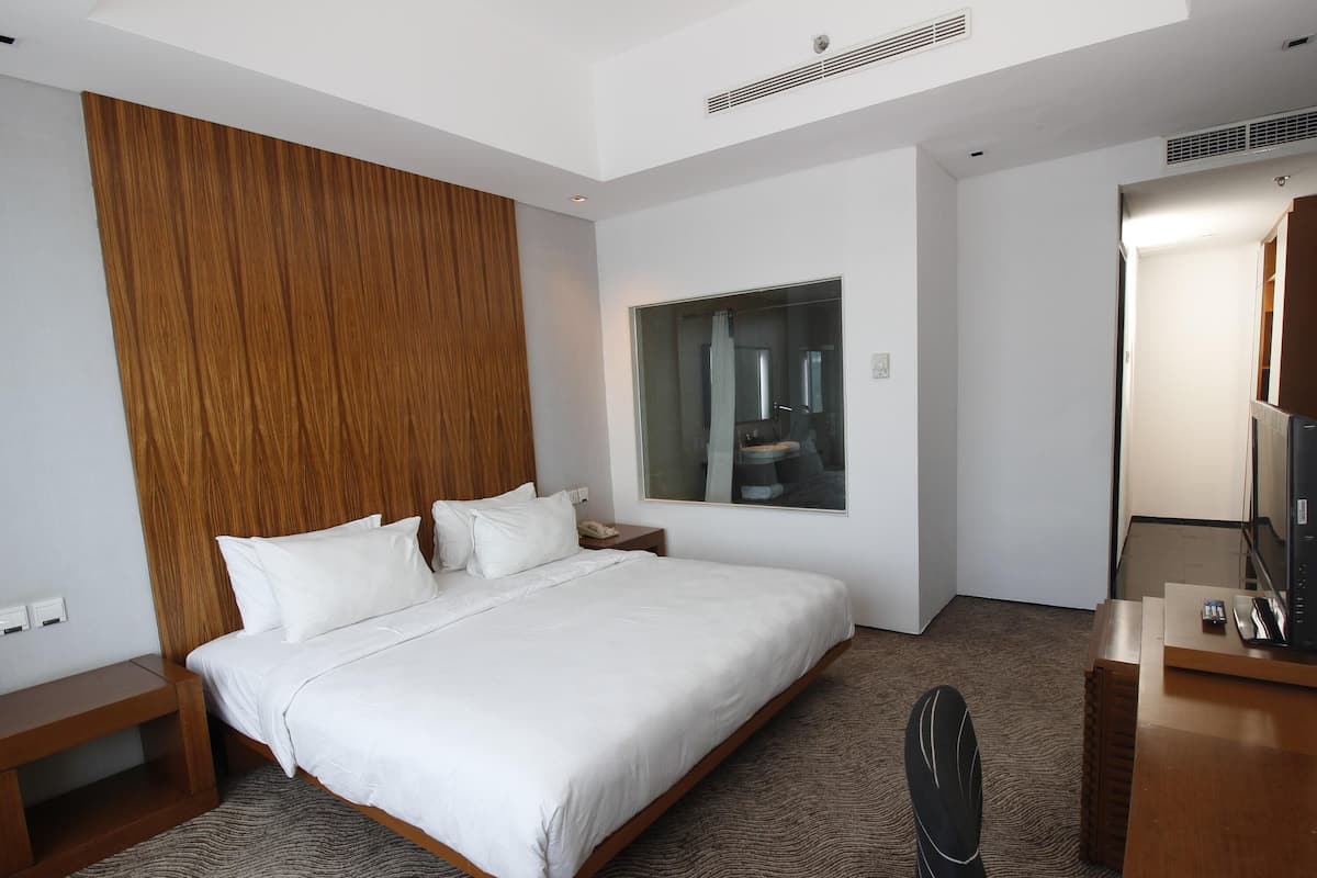 A hotel room with a large bed, a wooden headboard, a bedside table, a desk with a chair, a mirror, and a television.