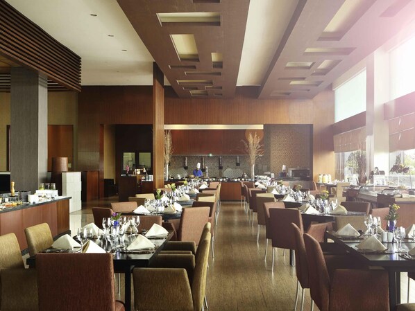 Un restaurant spacieux doté de nombreuses tables, d’un bar central et de grandes fenêtres laissant entrer la lumière naturelle.