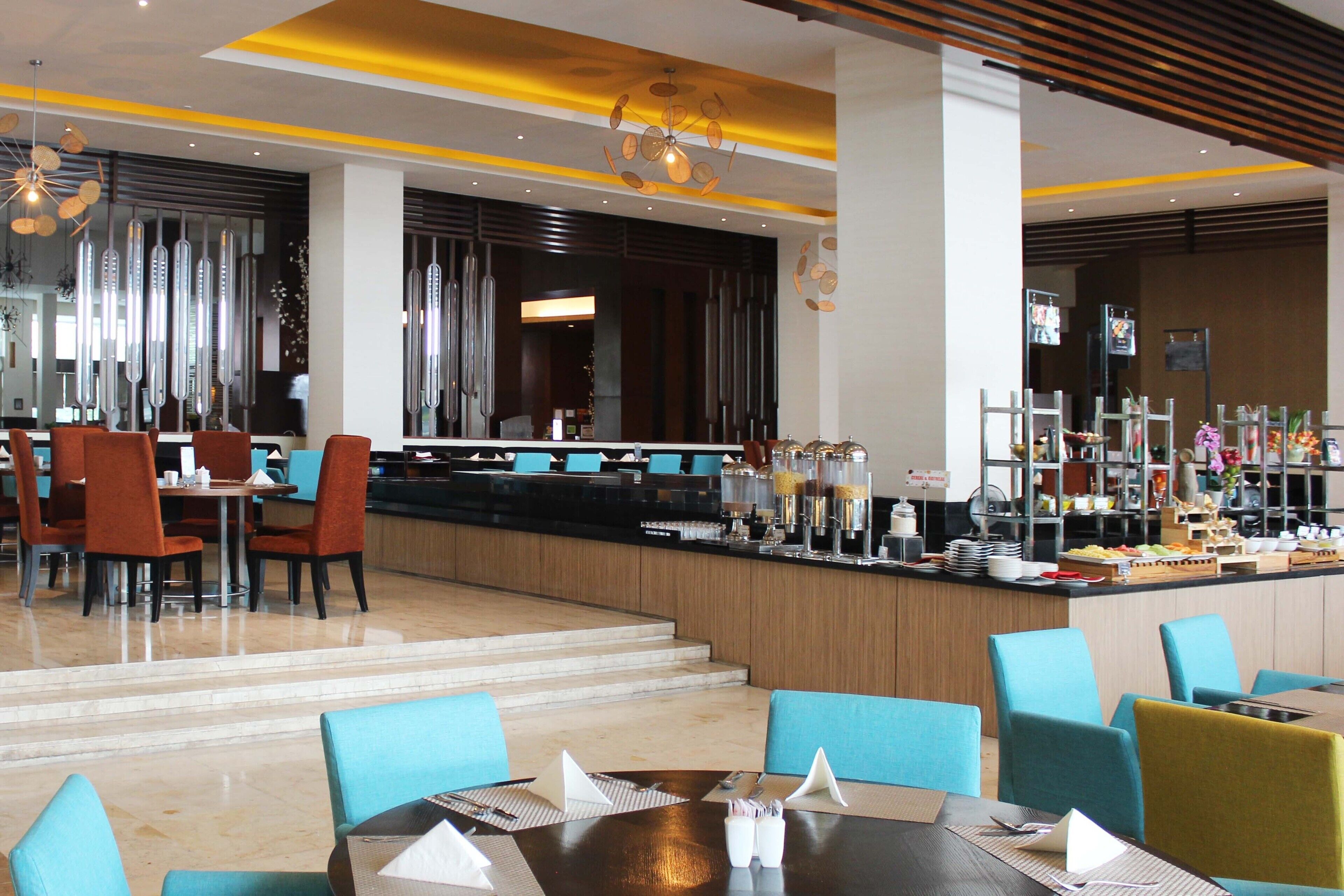A modern hotel lobby with a central bar area, seating arrangements, and a staircase leading to upper floors.