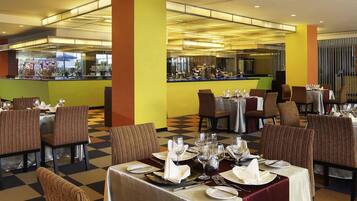 Een restaurant met meerdere tafels klaar voor het dineren, een bar en uitzicht op de keuken.