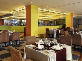 Een restaurant met meerdere tafels klaar voor het dineren, een bar en uitzicht op de keuken.