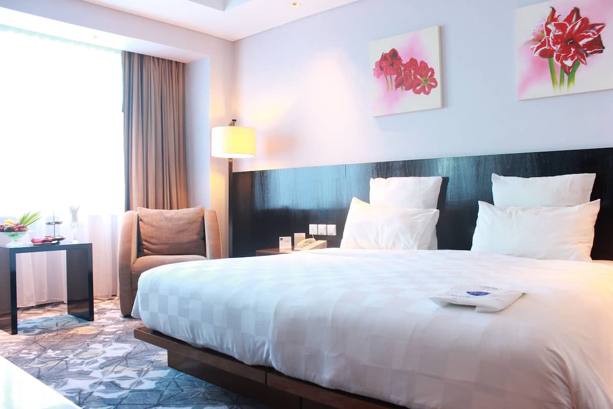 A hotel room with a large bed, a bedside table with a lamp, a chair, and artwork on the wall.