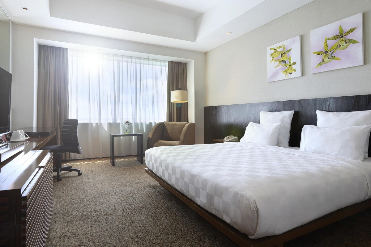 Une chambre d’hôtel avec un grand lit, un bureau avec une chaise, une télévision et une fenêtre avec des rideaux.