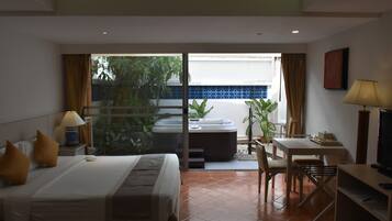 A hotel room with a bed, a desk, a chair, a TV, and a hot tub visible through a sliding door.