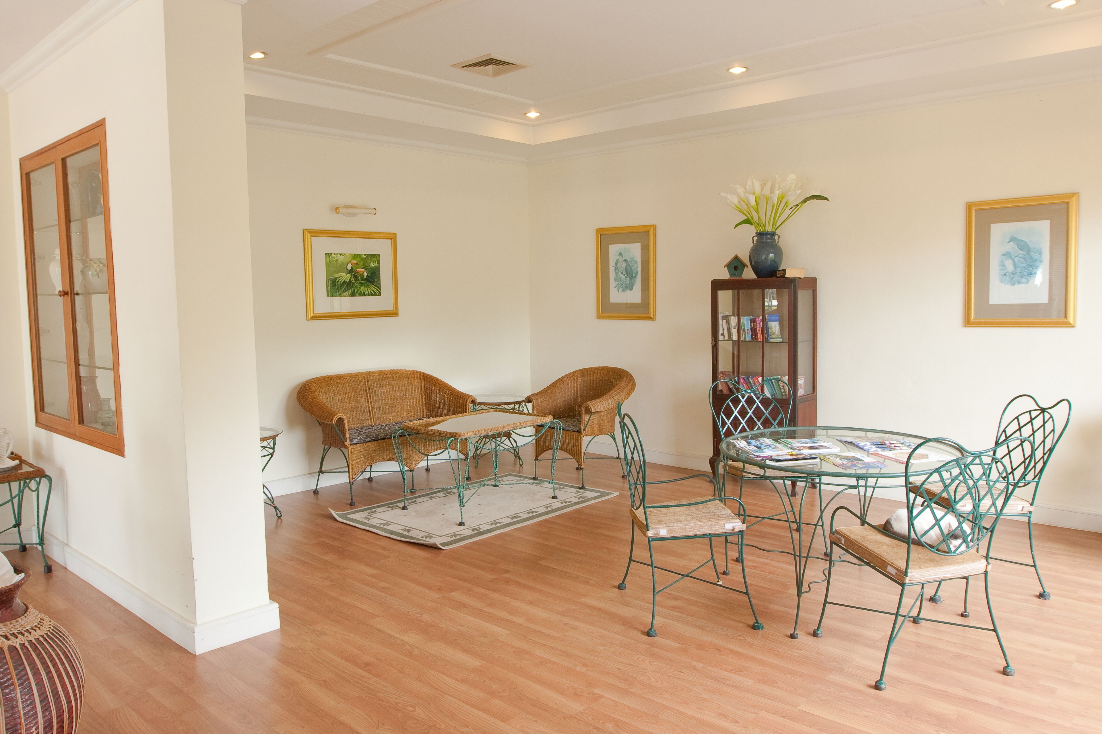 A dining area with wicker furniture, a glass table, and framed artwork on the walls.