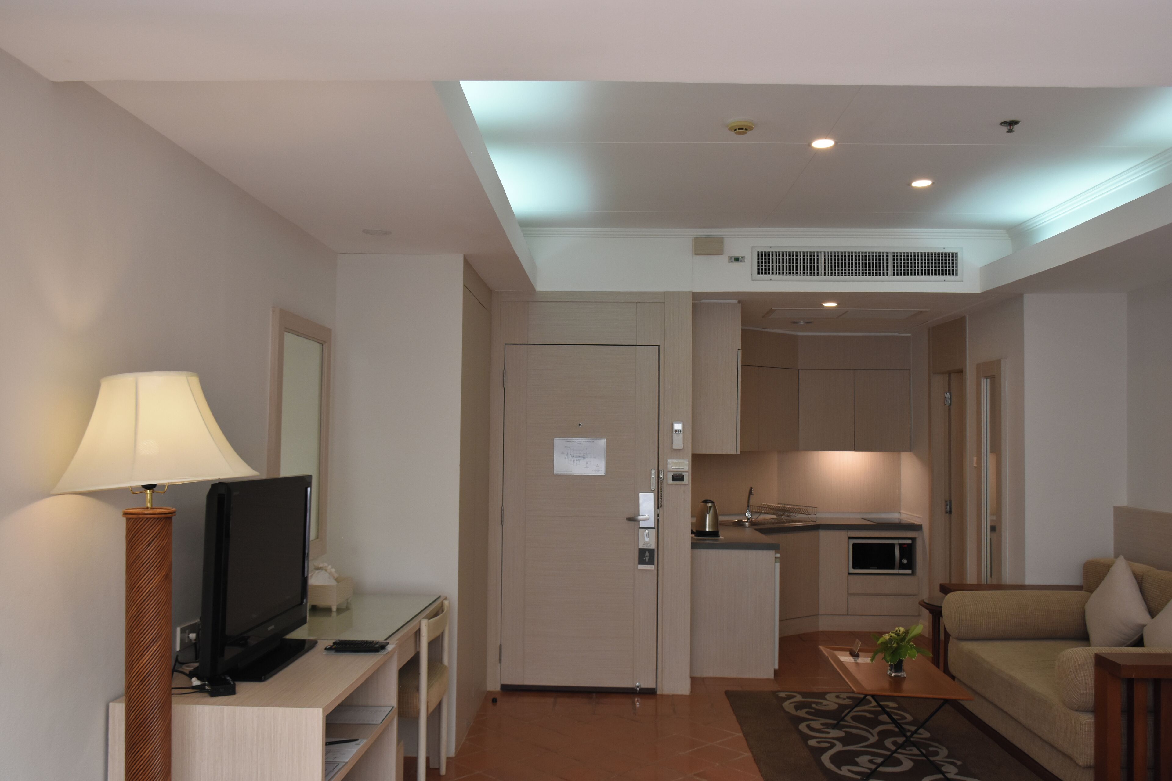 Une chambre d’hôtel moderne équipée d’un téléviseur à écran plat, d’une lampe, d’un canapé, d’une table basse et d’une kitchenette.