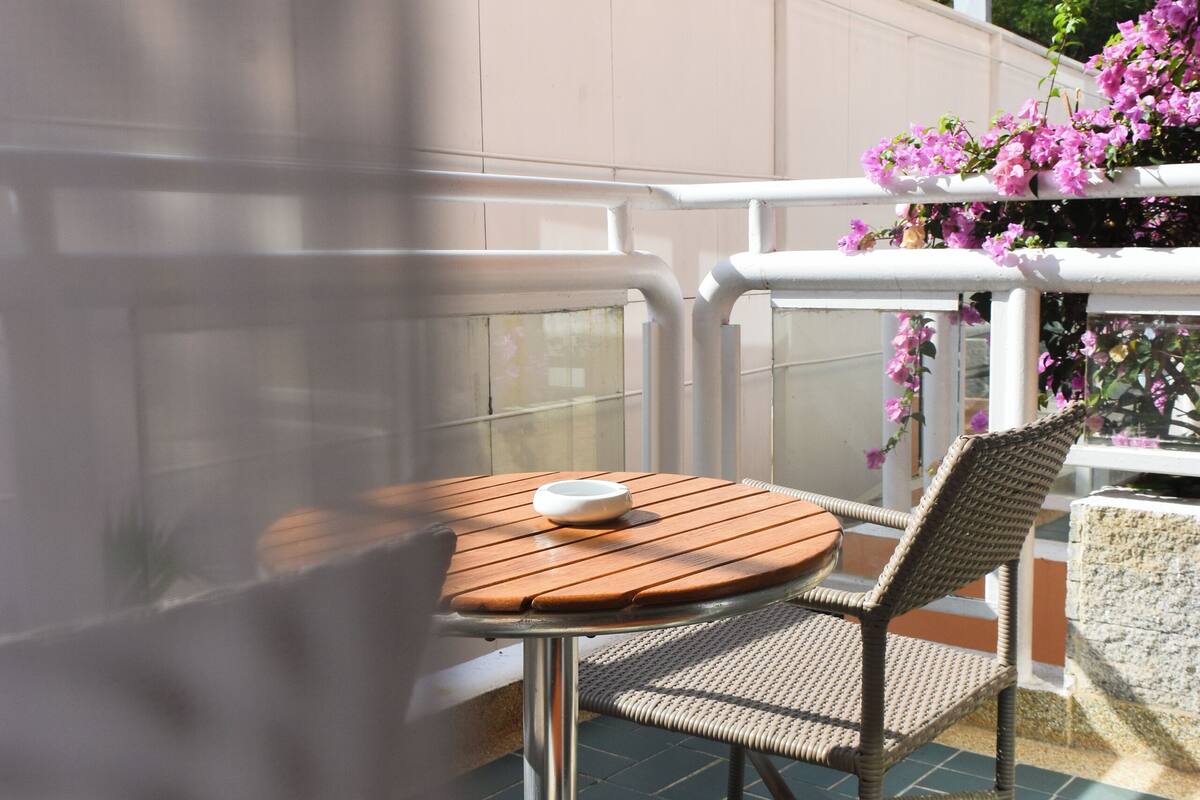 An outdoor patio with a round table and wicker chairs, surrounded by a white railing and a tiled floor.