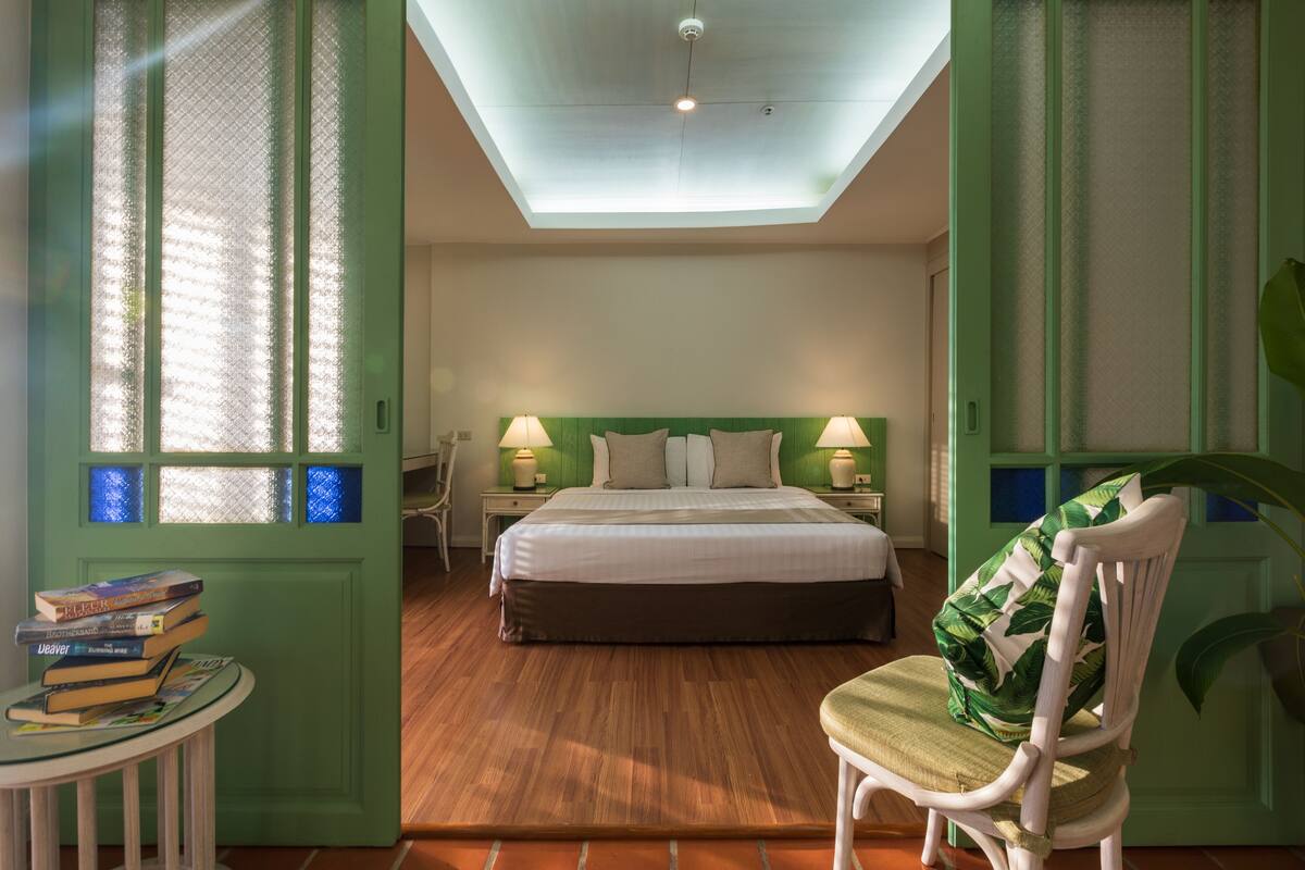 A bedroom with a bed, bedside lamps, a chair, and a small table with books.