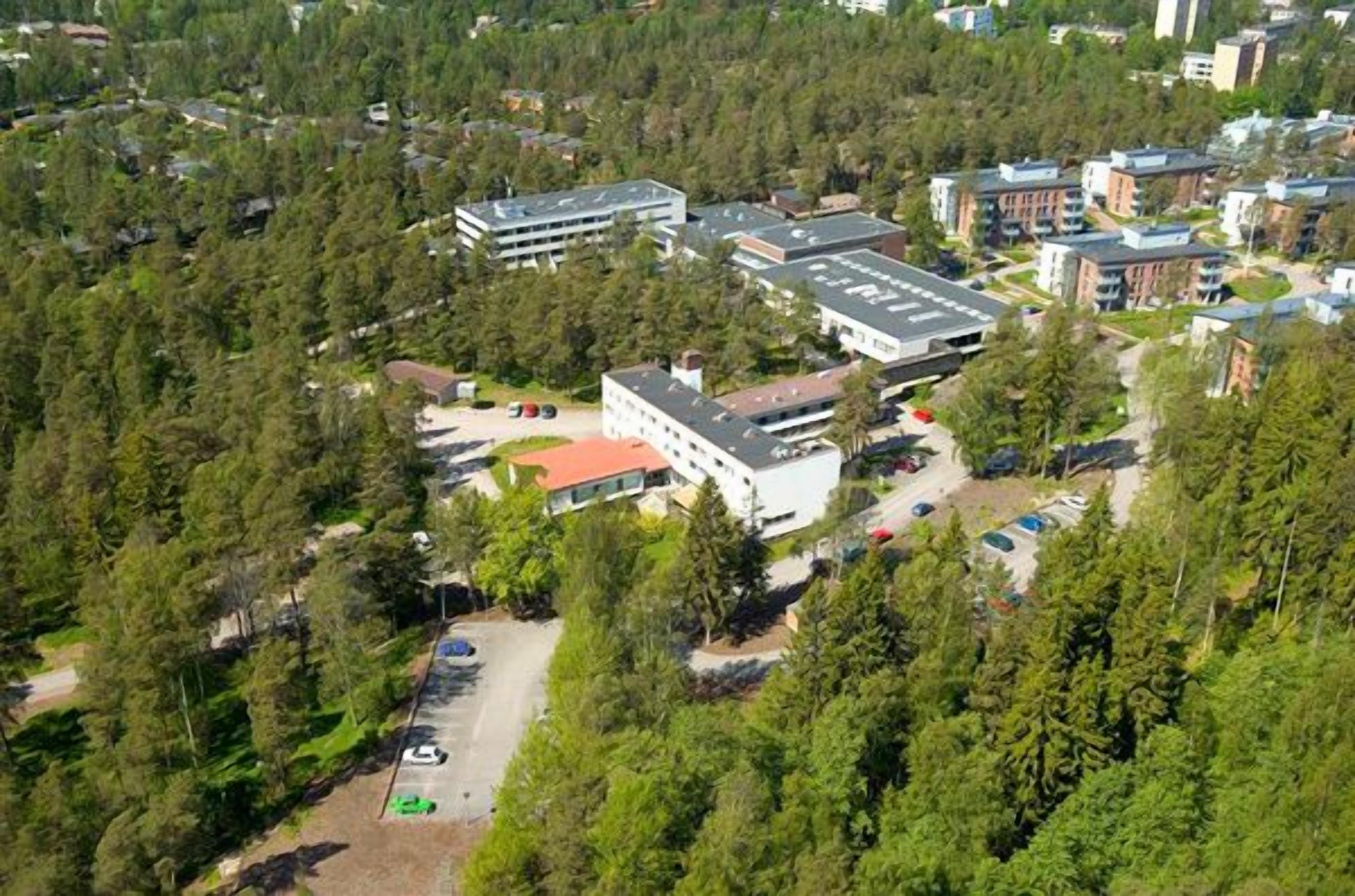 An aerial view of a campus with multiple buildings surrounded by dense forest.