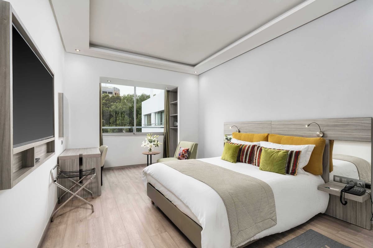 Una habitación de hotel moderna con una cama grande, un escritorio y una ventana con vistas a zonas verdes.
