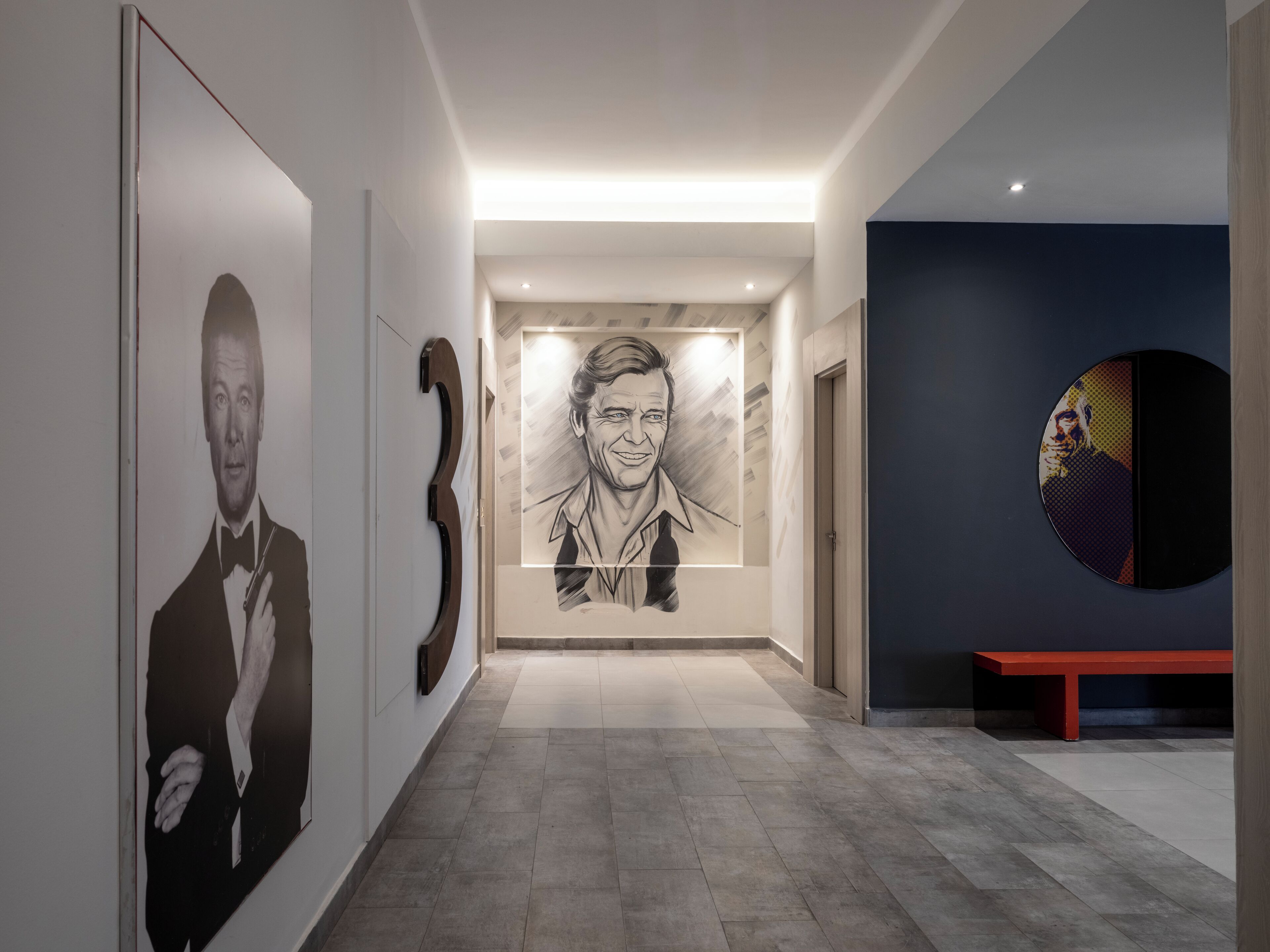 Un pasillo con diseño moderno, que incluye un retrato grande, una obra de arte original en la pared y un banco rojo.