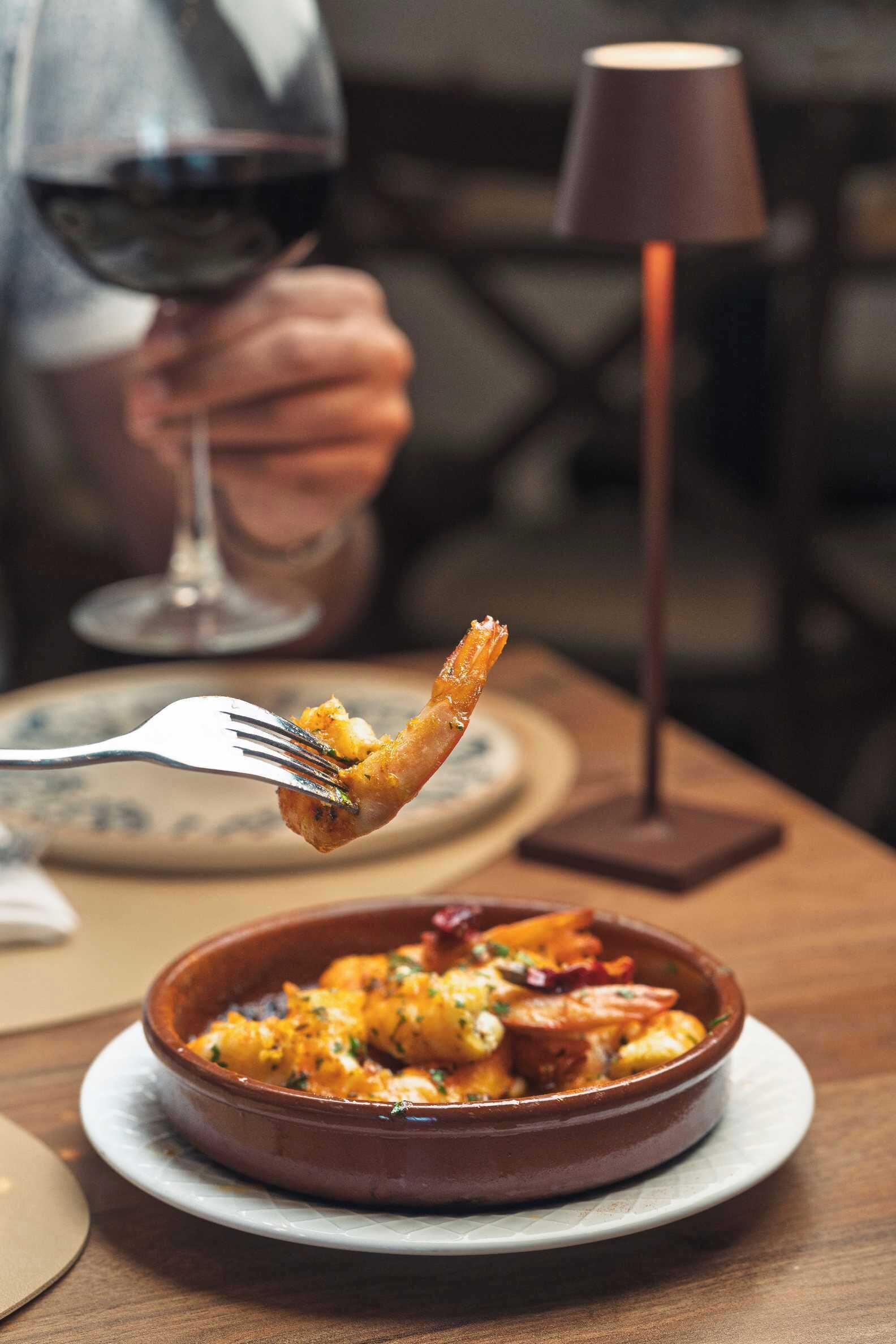 A dining table with a ceramic dish containing food, a wine glass, and a table lamp.