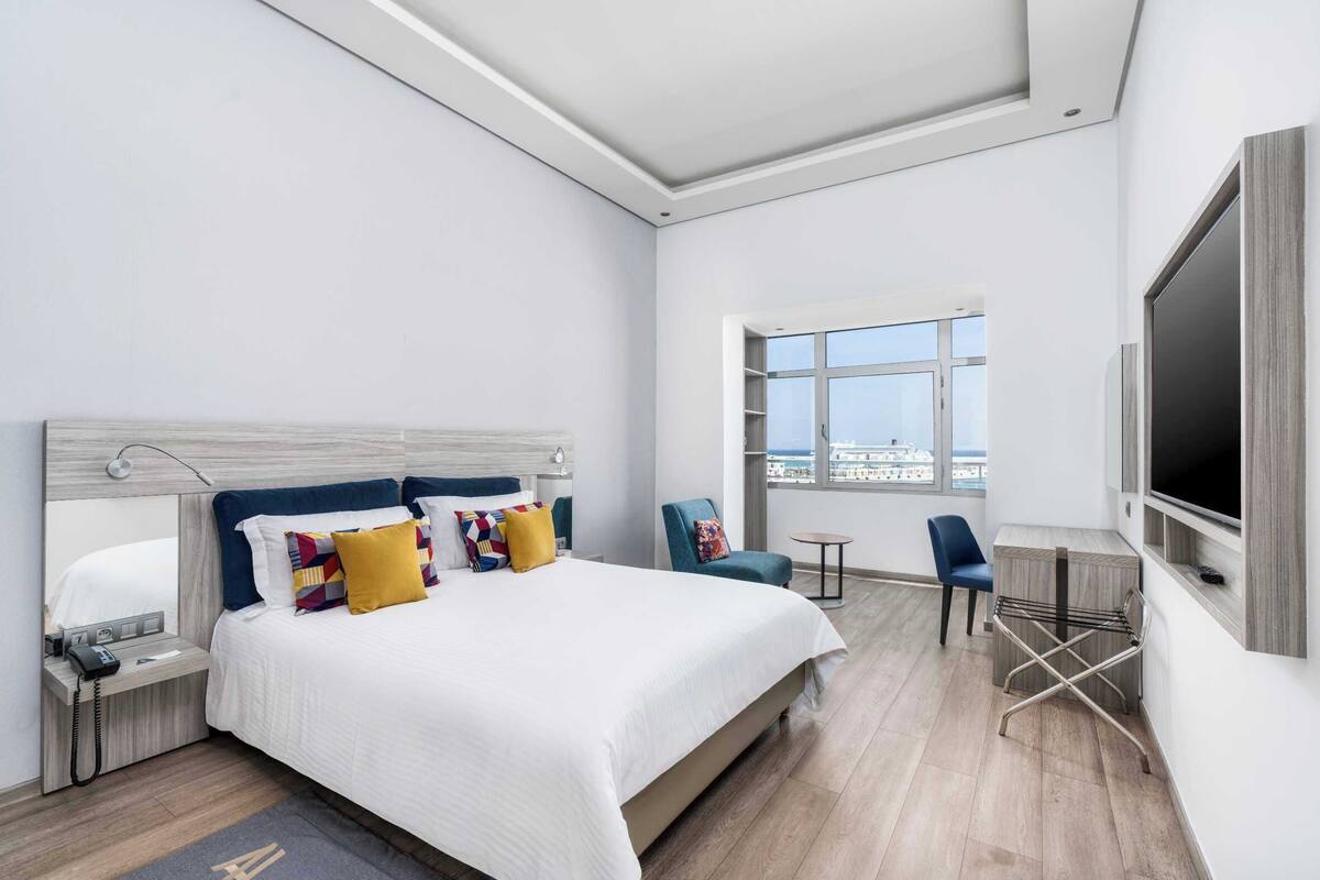 Una habitación de hotel moderna con una cama grande, un escritorio, una silla y un televisor.