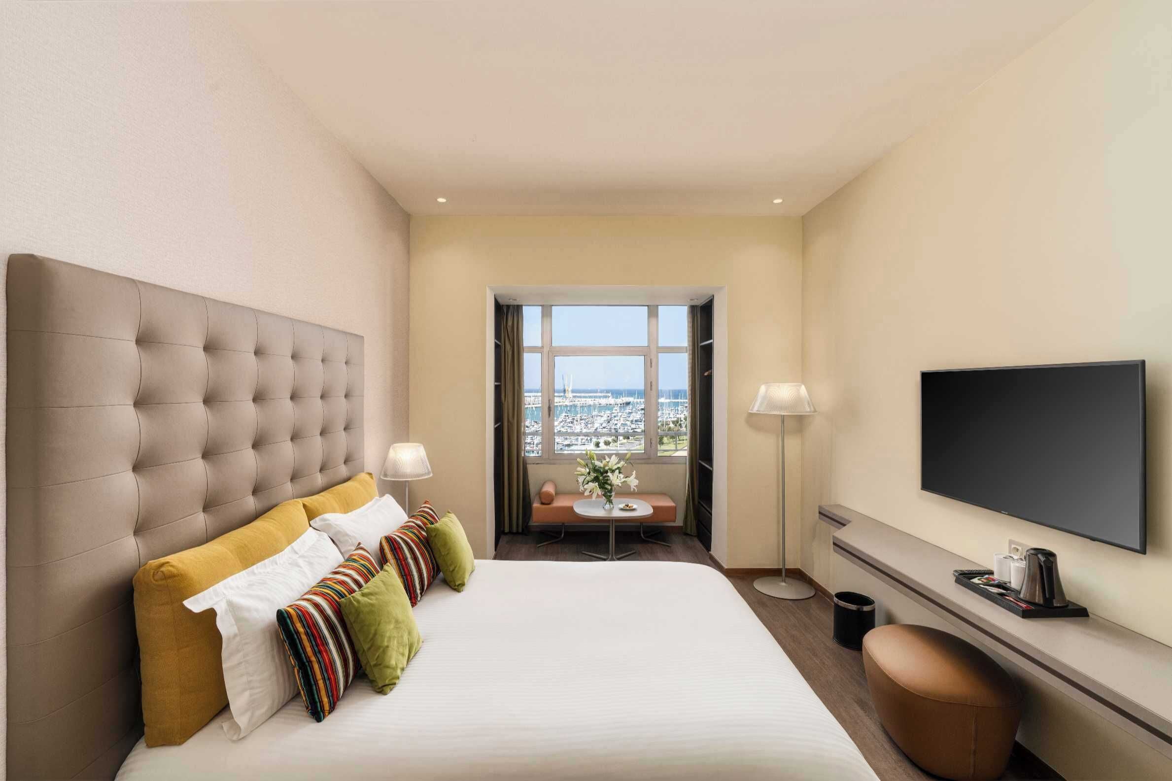 A hotel room with a large bed, a television, a seating area with a view, and a window.