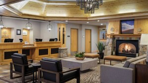 Een receptiebalie, een zithoek, een open haard en een houten plafond in de lobby.