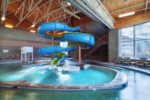 Une piscine intérieure dotée de plusieurs toboggans, d’un plafond en bois et de chaises disposées au bord du bassin.
