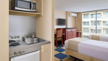 Una habitación de hotel con kitchenette, cama, escritorio y televisor.