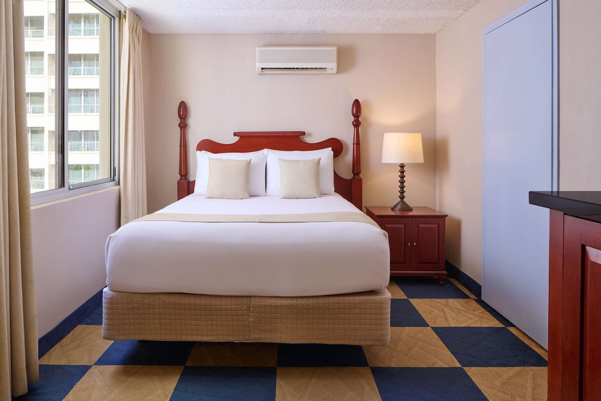 Une chambre d’hôtel avec un grand lit, une table de chevet avec une lampe, une armoire et une fenêtre avec des rideaux.