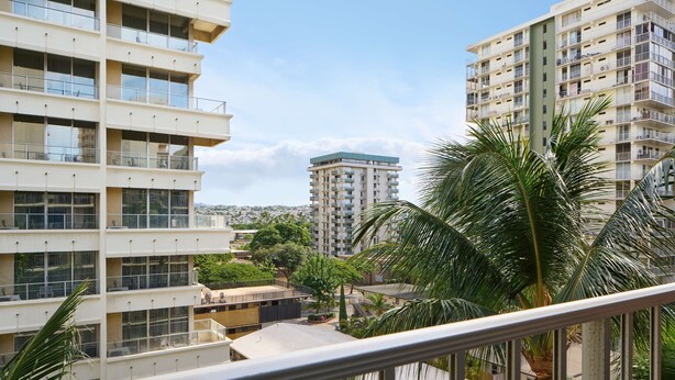 Un edificio residencial de varios pisos con balcones, un patio central y zonas verdes circundantes.