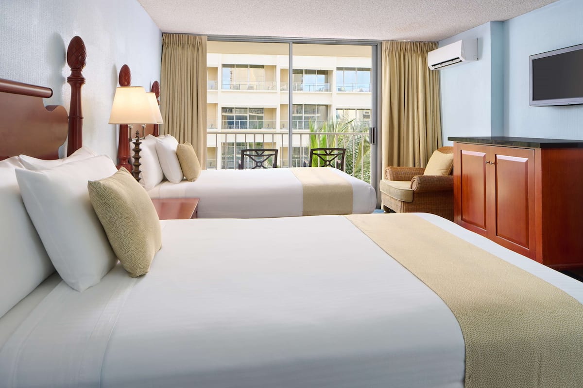 Une chambre d’hôtel avec deux lits, une télévision, un balcon donnant sur l’immeuble et un bureau avec une chaise.
