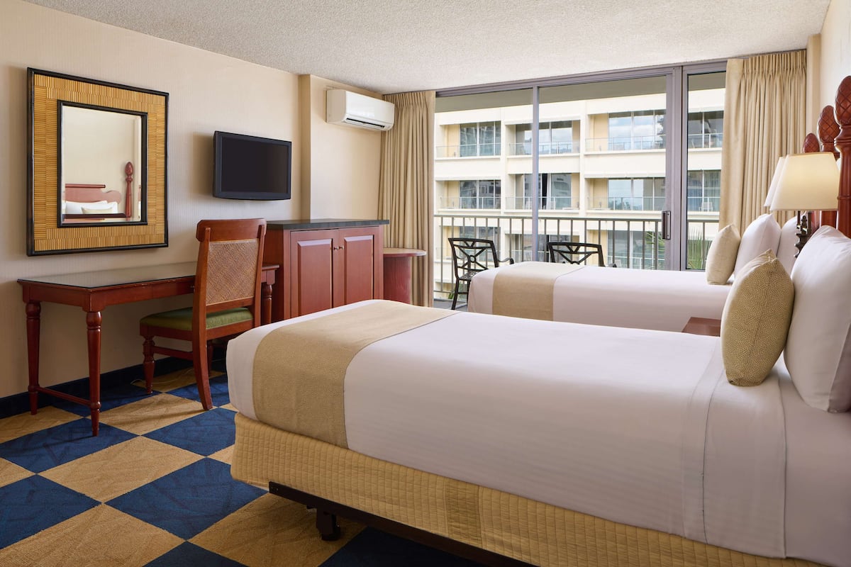 Une chambre d’hôtel avec deux lits, un bureau, une chaise, une télévision et un balcon donnant sur l’immeble.