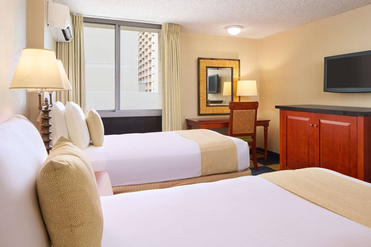Une chambre d’hôtel avec deux lits, un bureau, une chaise, une télévision et une fenêtre avec des rideaux.