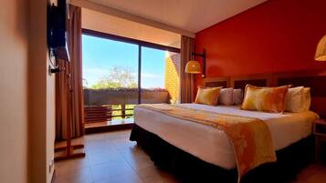 A bedroom with a large bed, a TV, a bedside table, and a view of the outdoors.