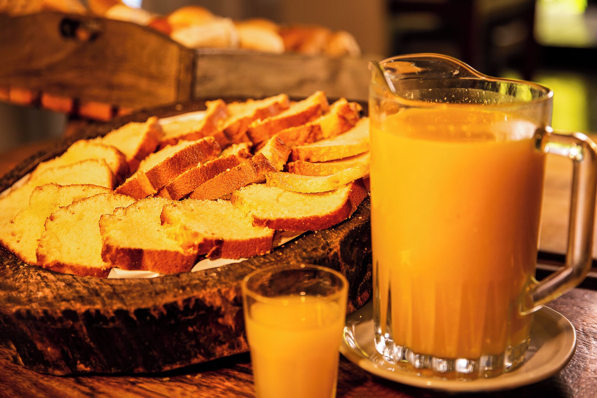 Une planche en bois servant de plateau, avec des tranches de pain et une carafe de jus d’orange.