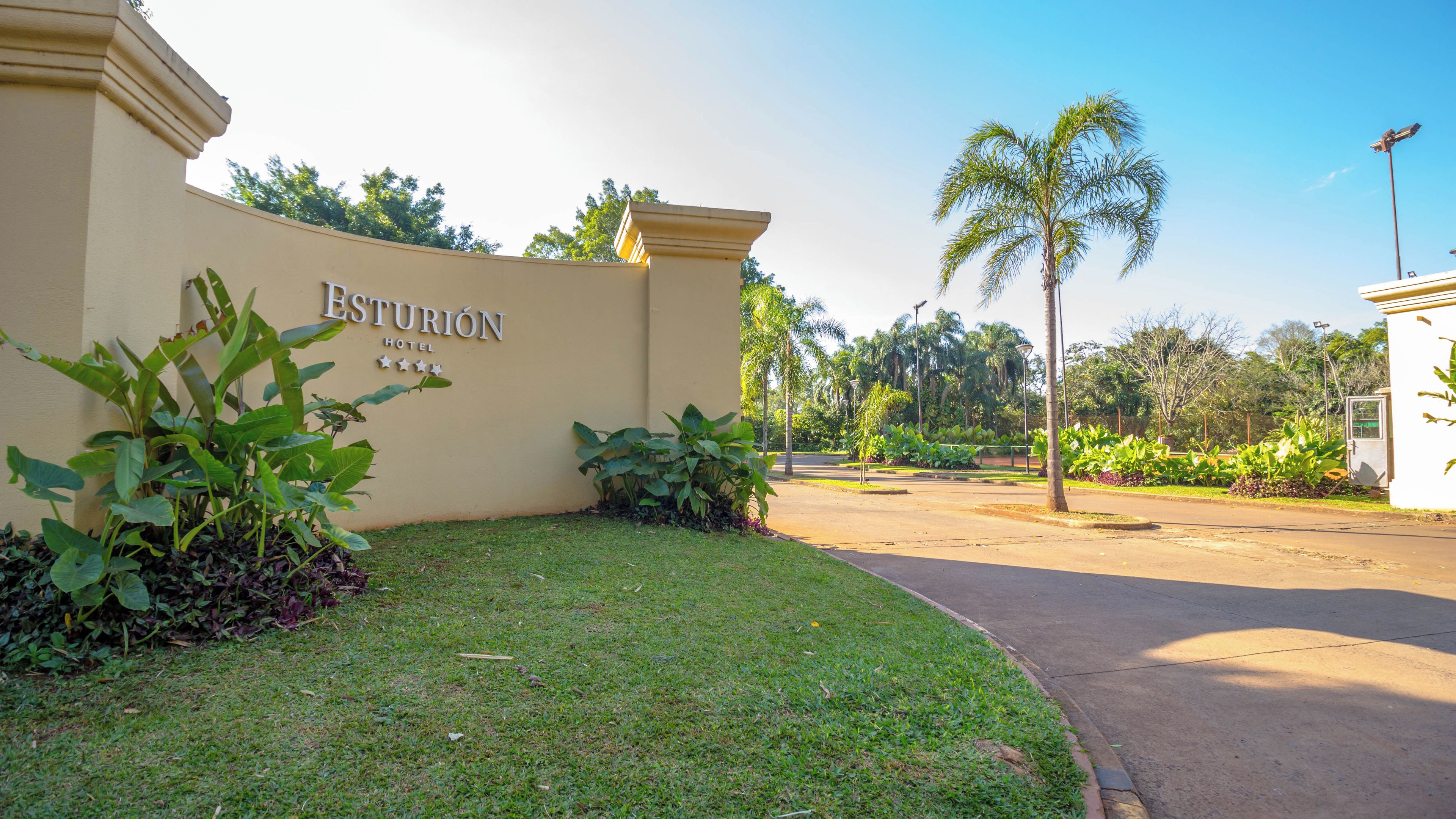A hotel entrance with a sign, a well-maintained lawn, and palm trees.