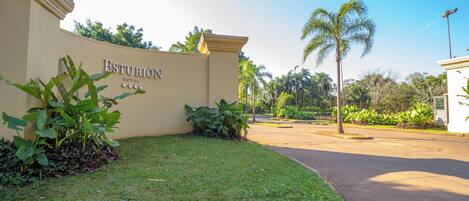A hotel entrance with a sign, a well-maintained lawn, and palm trees.