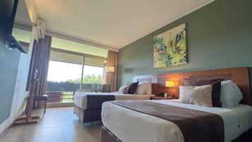 Habitación de hotel con dos camas, un ventanal grande, un cuadro en la pared y vistas al exterior con vegetación.