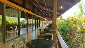 Un patio techado al aire libre con mesas y sillas, ventanas amplias y vistas a la vegetación.