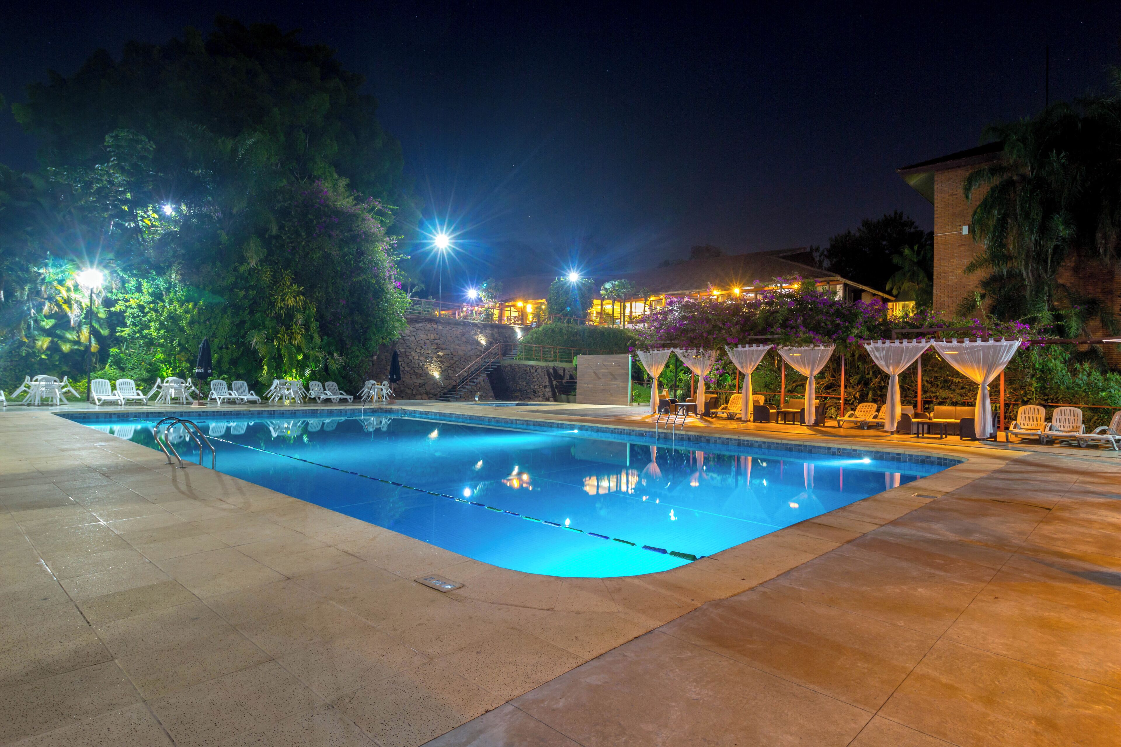 Una piscina con sillas de descanso y una zona de estar cubierta por la noche.