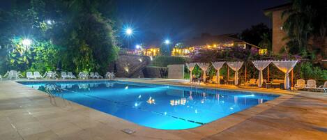 Una piscina con sillas de descanso y una zona de estar cubierta por la noche.