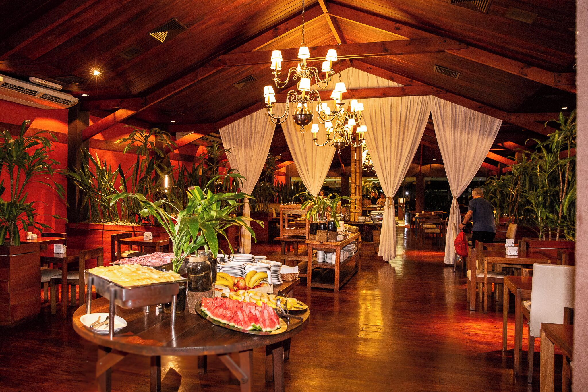 A restaurant with wooden tables, a chandelier, and a buffet with various food items.