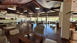 Un amplio espacio interior con piso de madera, múltiples disposiciones de asientos que incluyen sofás y sillones, e iluminación colgante.