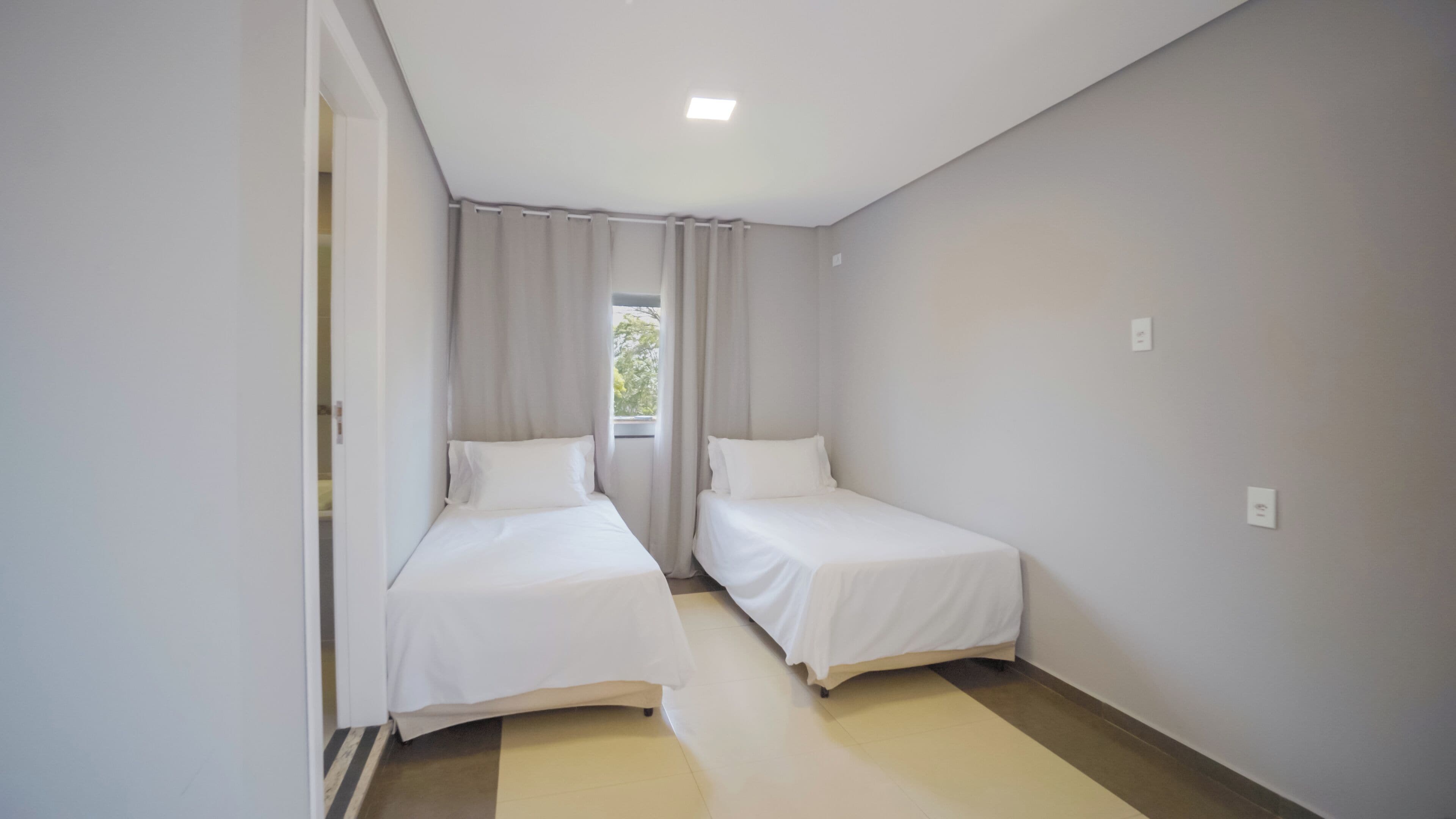 A small, clean room with two single beds, a window with curtains, and a ceiling light.